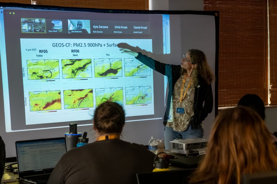 A scientist points to a slide projection of weather forecasts.