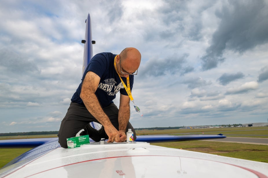 An aircraft mechanic kneels on the roof of the NSF NCAR C-130 to make repairs
