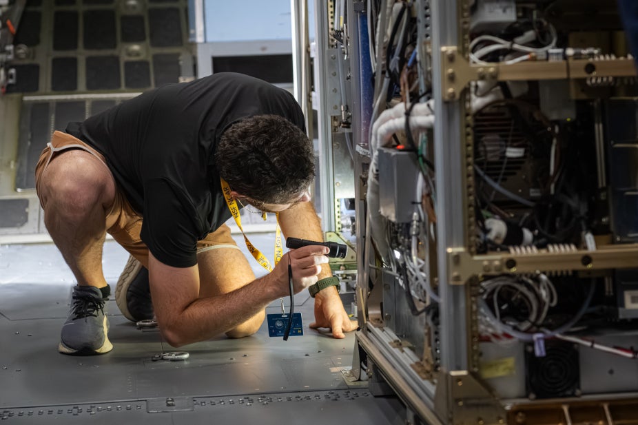 A technician crouches to inspect an instrument rack.