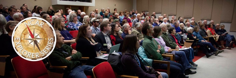 A large audience sits in an auditorium listening to a presenter