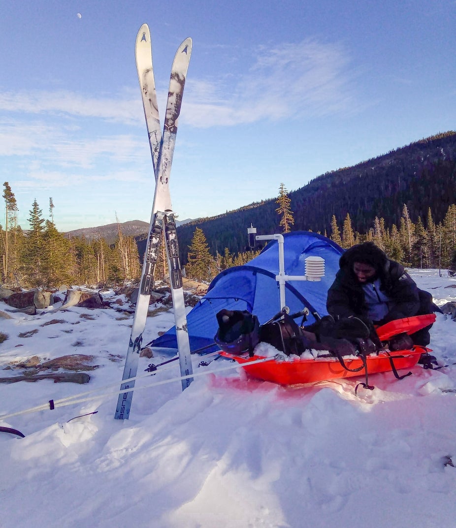 Agbeli with a mobile weather station in the snow with skis in the foreground.