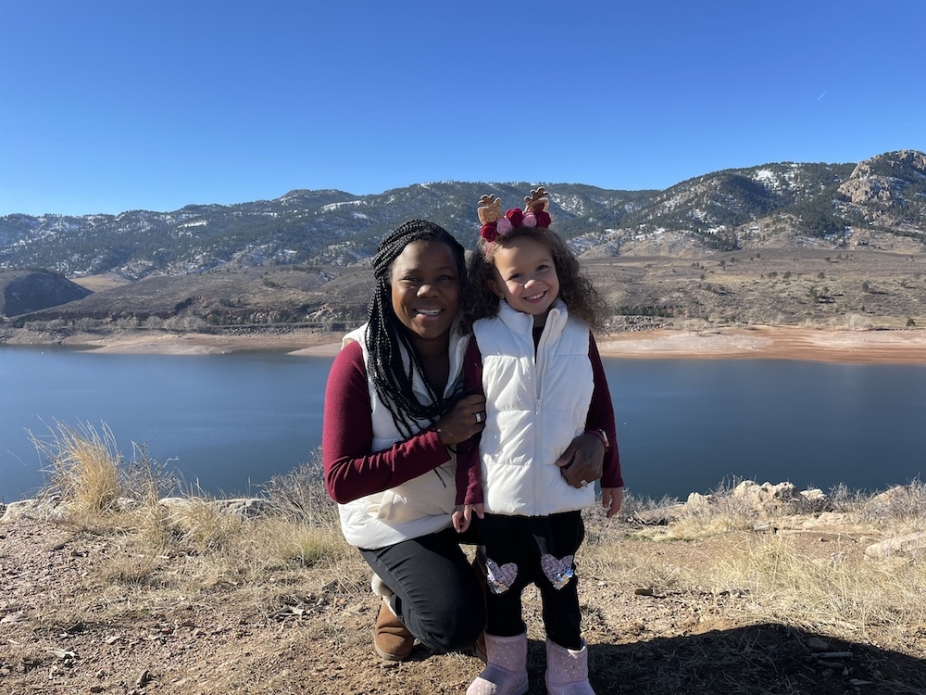 Melissa Burt with her daughter with a lake and foothills in the background.
