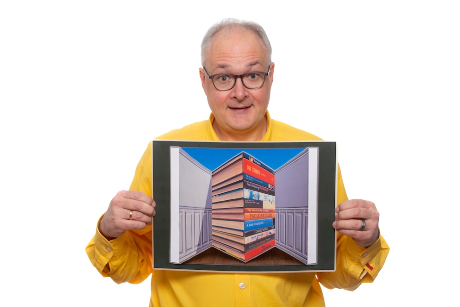 Scientist Jo Hecker holding an image showing forced perspectives of a stack of books in a room where the books appear larger than the walls.