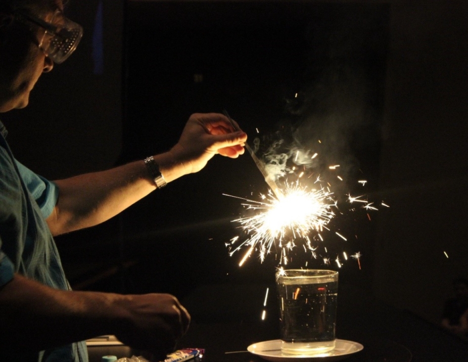 A man holds a sparkler over a mason jar filled with water.