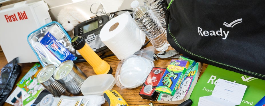 A countertop filled with emergency items including a first aid kit, toilet paper and a flash light. 
