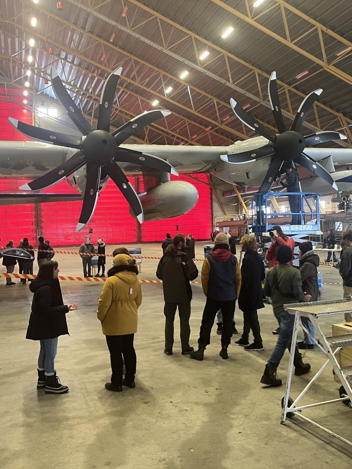 Members of a local community chat with a scientist as they wait to tour a research aircraft in a hangar