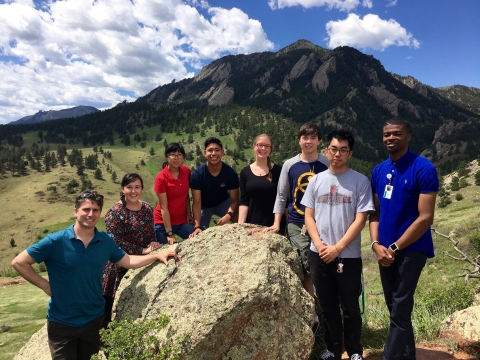 A group of students pose around a rock outside with mountains in the background