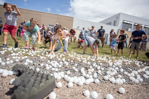 Elementary school kids race around a field to collect ping pong balls