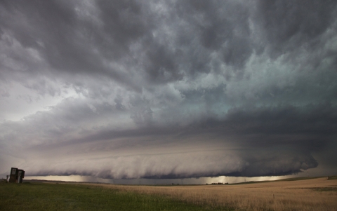 A large wall cloud arcs around a rotating thunderstorm updraft over an open field