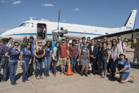 A large group of students, scientists, and elected officials pose in front of a research plane