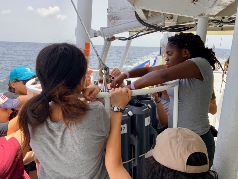 REU students work together on a research ship to prepare an oceanographic instrument