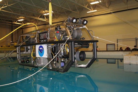 A remotely operated vehicle (ROV) is suspended above a water tank before testing