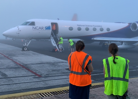 Scientists and engineers stand on the tarmac in front of a plane on a foggy morning.