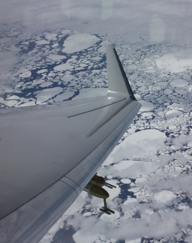An airplane wing with an atmospheric instrument flies over an icy sea