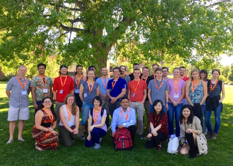 A group of postdoctoral fellows pose on a lawn surround by trees