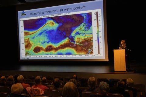 A scientist presents from a lecturn in front of an auditorium crowd