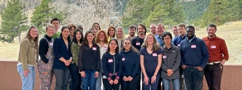 A large group of early careers pose in front of a forested background