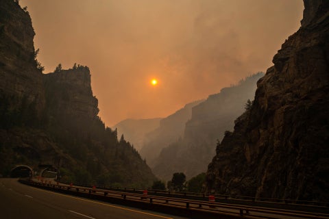 A sun blazing orange through smoke-covered skies, flanked by Colorado hills.