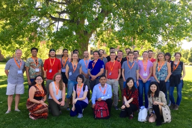 A group of postdoctoral fellows pose on a lawn surround by trees
